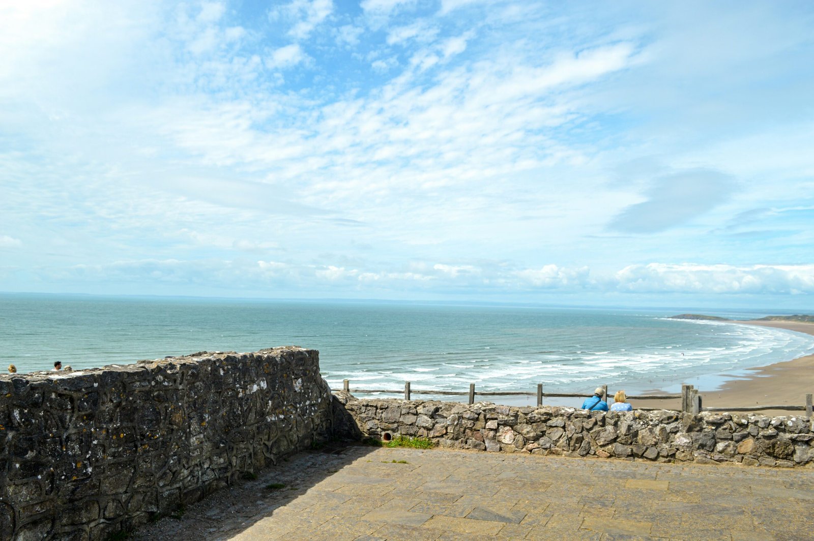 a stone wall next to the ocean with people sitting on it