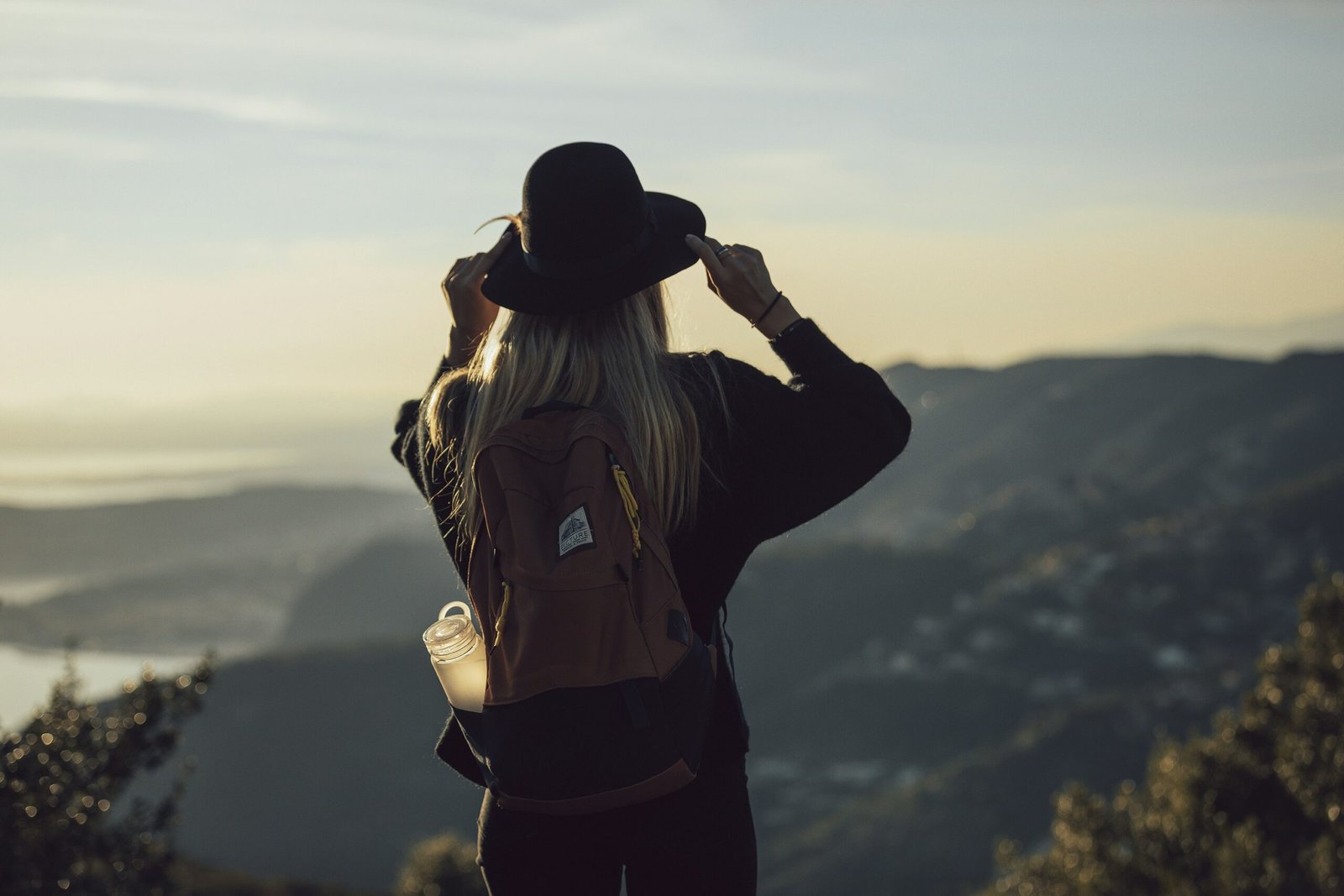 woman in gray hoodie woman in gray hoodie and black pants wearing black hat standing on top of mountain during